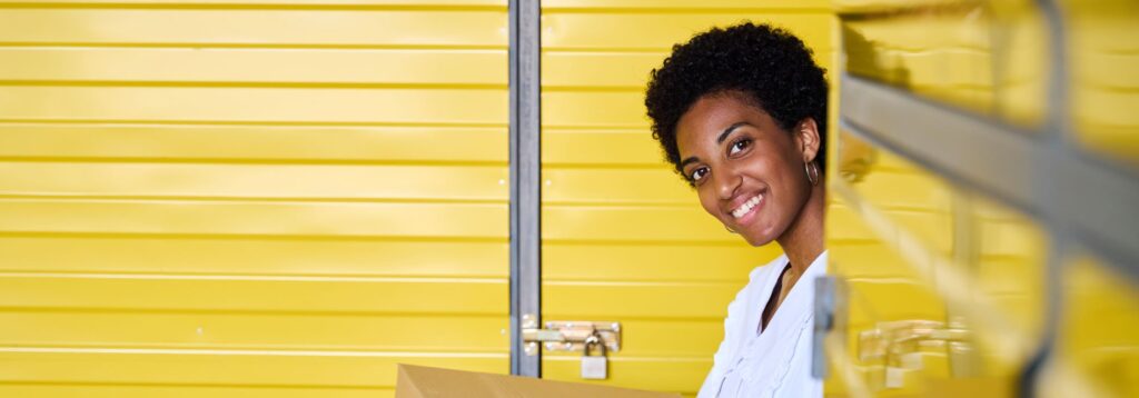 smiling-young-woman-standing-in-warehouse-with-car-2024-10-18-08-53-30-utc (2) | Best Dubai Storage flexible rental self torage